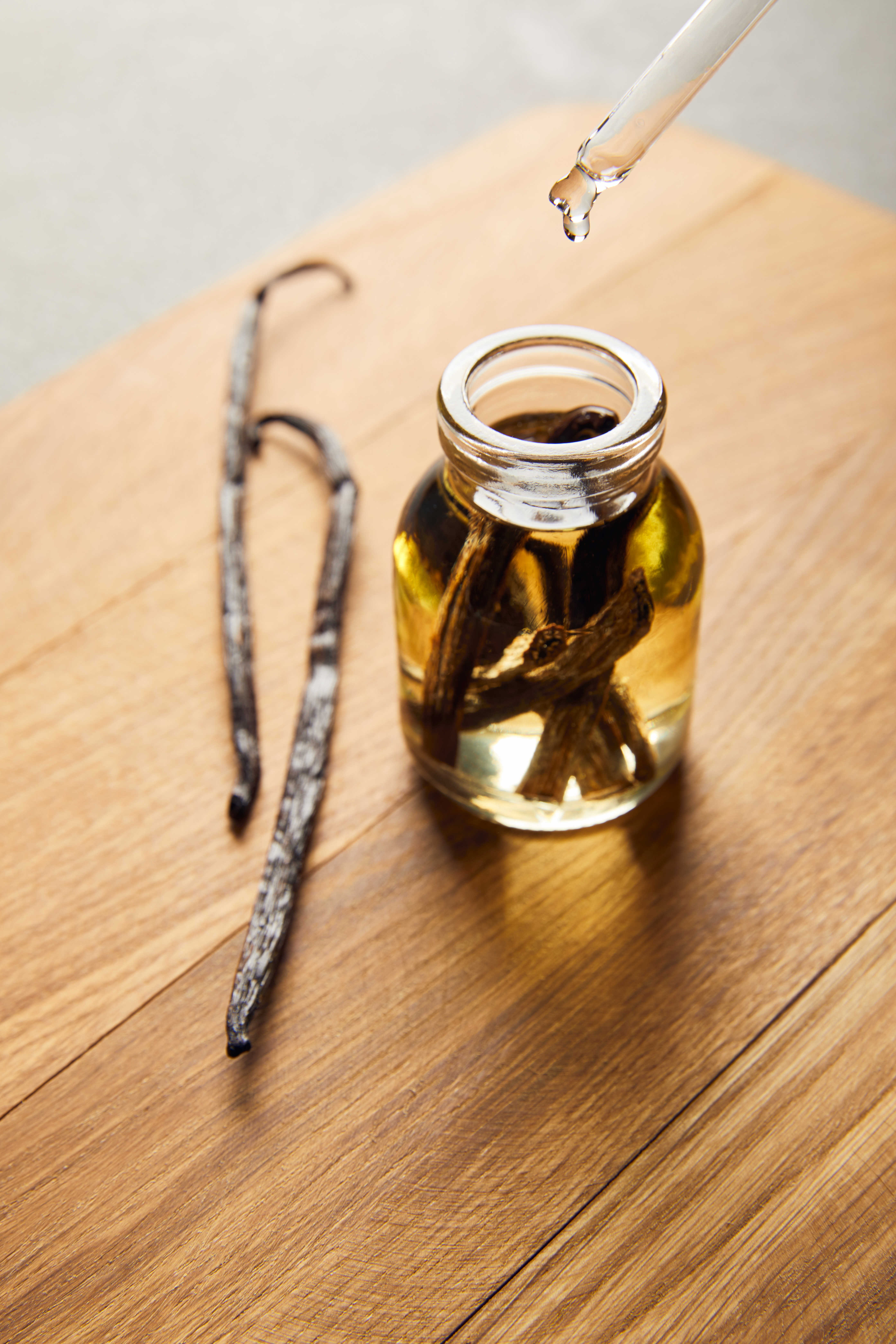 Glass bottle of essential oil with vanilla pods on wooden cutting board